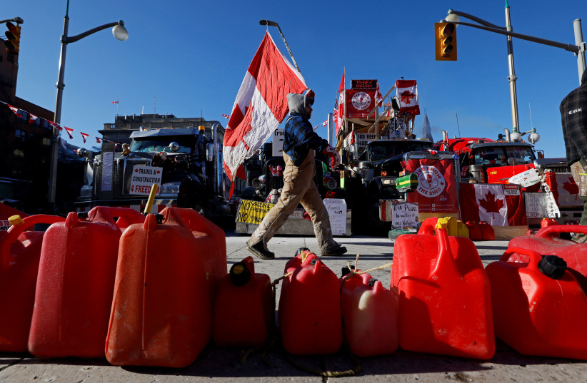  A demonstrator holding a Canadian flag walks in front of vehicles as truckers and their supporters block downtown streets as they continue to protest the coronavirus disease (COVID-19) vaccine mandates, in Ottawa, Ontario, Canada, February 14, 2022. (photo credit: REUTERS/BLAIR GABLE)