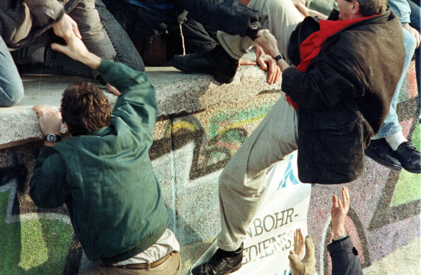 EAST GERMAN citizens climb the Berlin Wall after the East German border opened in 1989. Like many Germans, the family of the author, who grew up in Moscow as the USSR-East Germany collapsed, was split by geopolitical borders and war. (photo credit: REUTERS)