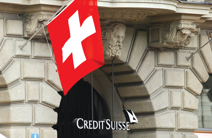  SWITZERLAND’S NATIONAL flag flies above the logo of Swiss bank Credit Suisse at its headquarters in Zurich.  (photo credit: ARND WIEGMANN / REUTERS)