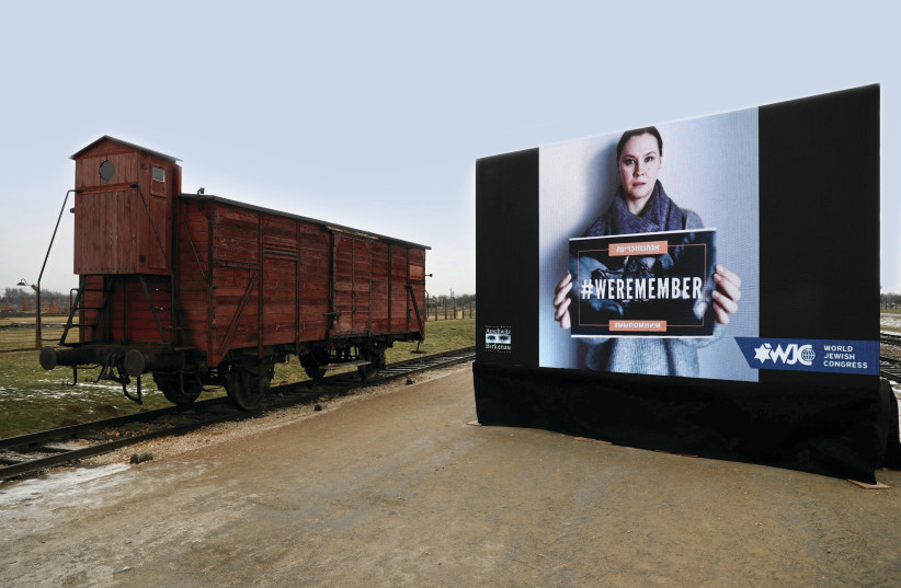  A train car and a World Jewish Congress screen display are seen at Auschwitz-Birkenau during ceremonies marking the 77th anniversary of the liberation of the camp and International Holocaust Remembrance Day on January 27, 2022.  (credit: Jakub Porzycki/Agencja Wyborcza/Reuters)