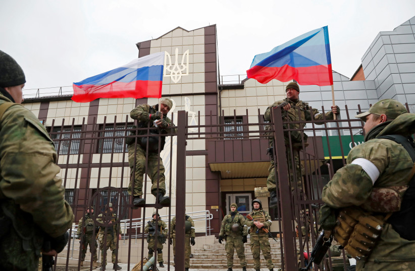  Servicemen of pro-Russian militia hoist flags of Russia and the separatist self-proclaimed Luhansk People's Republic (LNR) outside the Oschad bank branch in Stanytsia Luhanska in the Luhansk region, Ukraine February 27, 2022. (photo credit: REUTERS/ALEXANDER ERMOCHENKO)