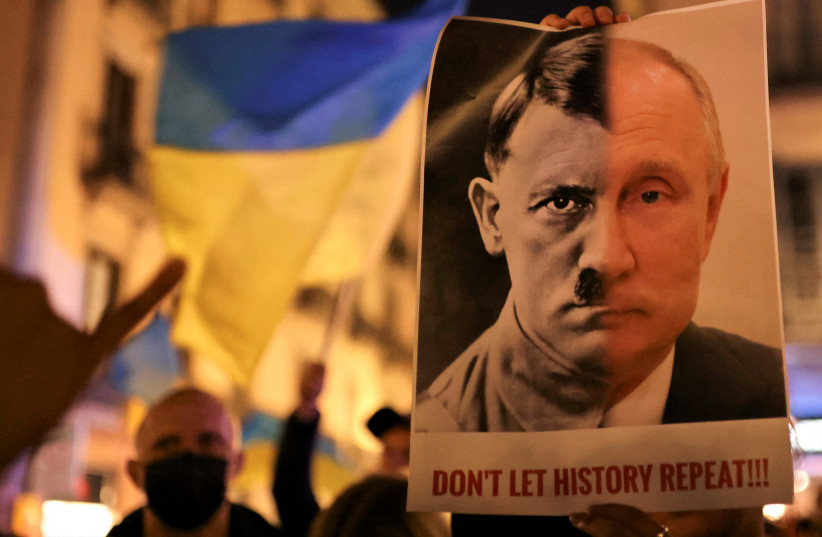  A person holds a banner with the joined faces of a portrait of Vladimir Putin and Nazi dictator Adolf Hitler during an anti-war protest, after Russian President Vladimir Putin authorised a massive military operation against Ukraine, in Barcelona, Spain, February 24, 2022 (photo credit: NACHO DOCE/REUTERS)
