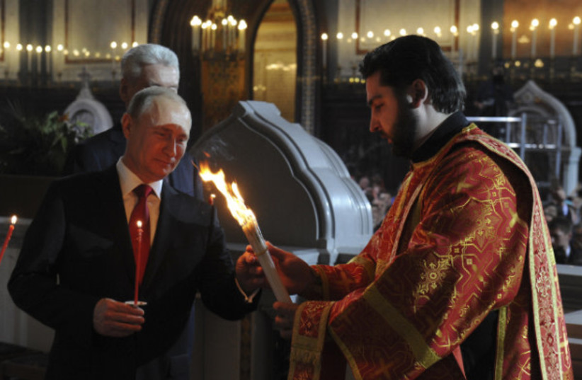 Russian President Vladimir Putin takes lighted candles from a priest during an Orthodox Easter service in the Christ the Saviour Cathedral in Moscow, April 20, 2014. (photo credit: REUTERS/Mikhail Klimentyev/RIA Novosti/Kremlin)