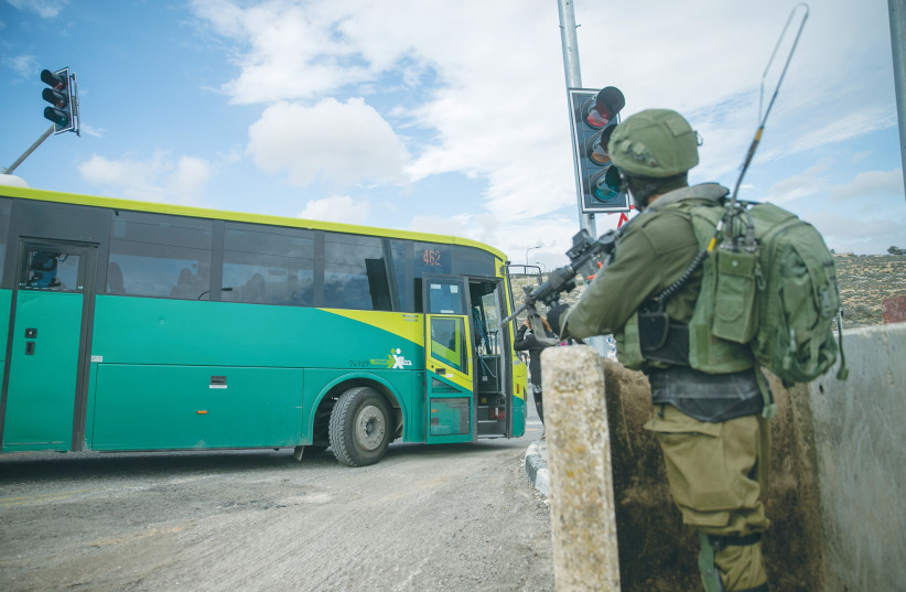  SOLDIERS GUARD a bus stop at the entrance to the Givat Assaf outpost near Ramallah, in this 2018 photo. (photo credit: YONATAN SINDEL/FLASH90)