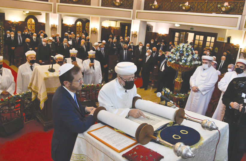  PRESIDENT ISAAC HERZOG holds one of the handles of the Torah scroll at the Neve Shalom Synagogue in Turkey.  (photo credit: HAIM ZACH/GPO)