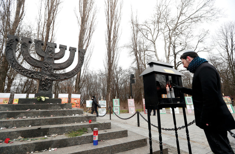  A MAN places a candle next to a monument in Kyiv commemorating the victims of Babyn Yar.  (credit: VALENTYN OGIRENKO/REUTERS)