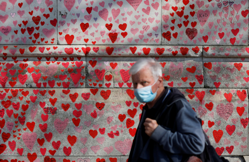  A man wearing a face-mask walks past The National Covid Memorial Wall, on national day of reflection to mark the two year anniversary of the UK going into national lockdown, in London (photo credit: REUTERS/PETER CZIBORRA)