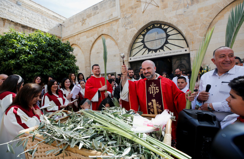  Father Rami Asakriyah sprinkles holy water on palm fronds during the Palm Sunday service at the Church of the Nativity in Bethlehem, in the West Bank, April 10, 2022. (photo credit: MUSSA QAWASMA/REUTERS)