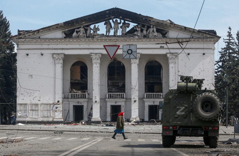  A woman walks next to an armored vehicle of pro-Russian troops the building of a theatre destroyed in the course of Ukraine-Russia conflict in the southern port city of Mariupol, Ukraine April 10, 2022.  (credit: REUTERS/ALEXANDER ERMOCHENKO)