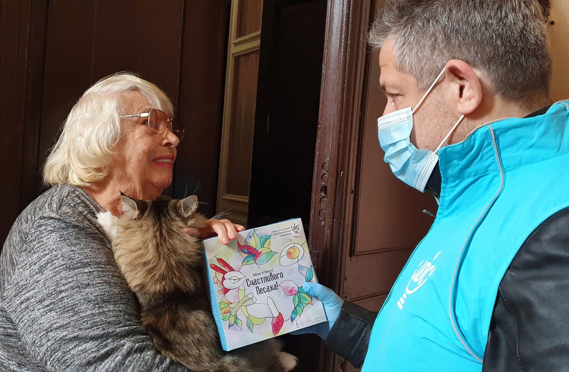  Svetlana Niselevitch receives a haggadah for Passover from a JDC staff member outside her home in Odessa, Ukraine, April 8, 2022.  (photo credit: JDC)