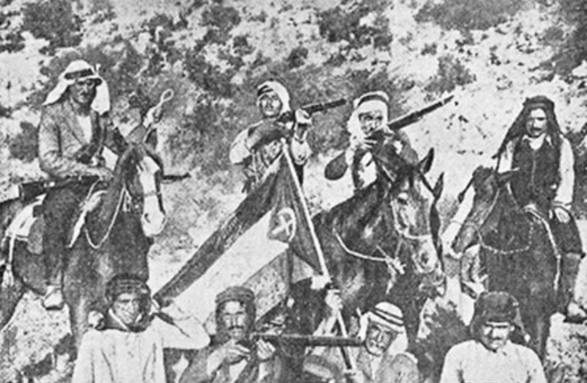  Arab rebels from the Haifa area and hills around Jenin posing with their commander, Abd al-Qadir Yusuf Abd al-Hadi. One rebel is carrying a Palestinian flag with a crescent and cross emblazoned on it. (credit: Wikimedia Commons)