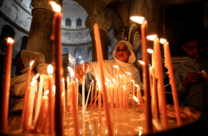  A Christian worshiper lights candles as she attends Easter Sunday Mass in the Church of the Holy Sepulchre in Jerusalem's Old City April 17, 2021. (photo credit: AMIR COHEN/REUTERS)