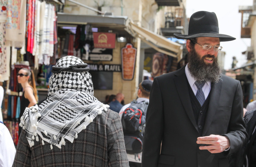 A Palestinian man and an Israeli Ultra-Orthodox Jew are seen walking in Jerusalem's Old City on April 17, 2022 (credit: MARC ISRAEL SELLEM/THE JERUSALEM POST)