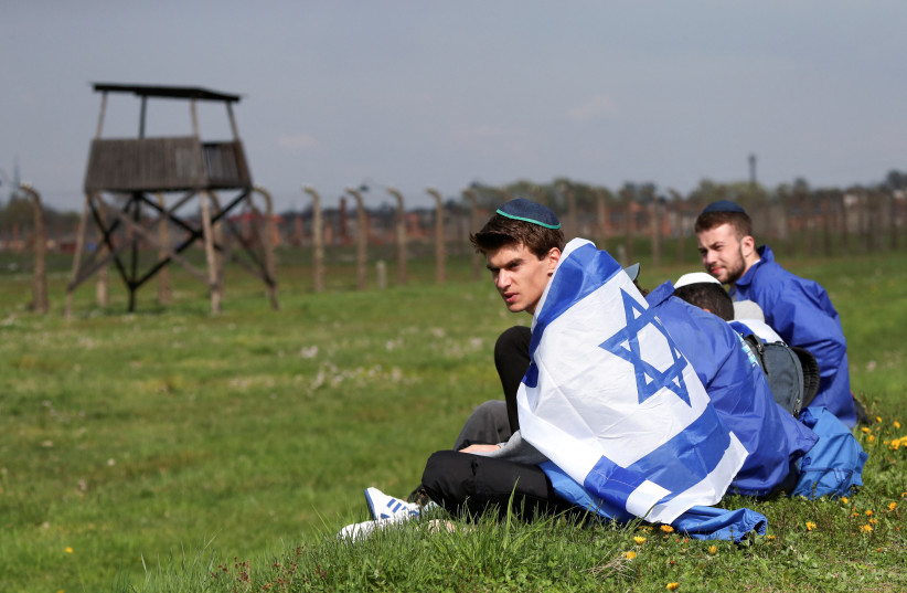  Men wearing kippah look on as they sit on the ground during the annual International "March of the Living" at the former Auschwitz II-Birkenau death camp, in Brzezinka near Oswiecim, Poland April 28, 2022. (photo credit: REUTERS/KACPER PEMPEL)