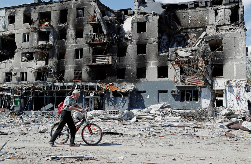  A local resident walks with his bicycle near a destroyed apartment building in Mariupol. (credit: REUTERS/ALEXANDER ERMOCHENKO)
