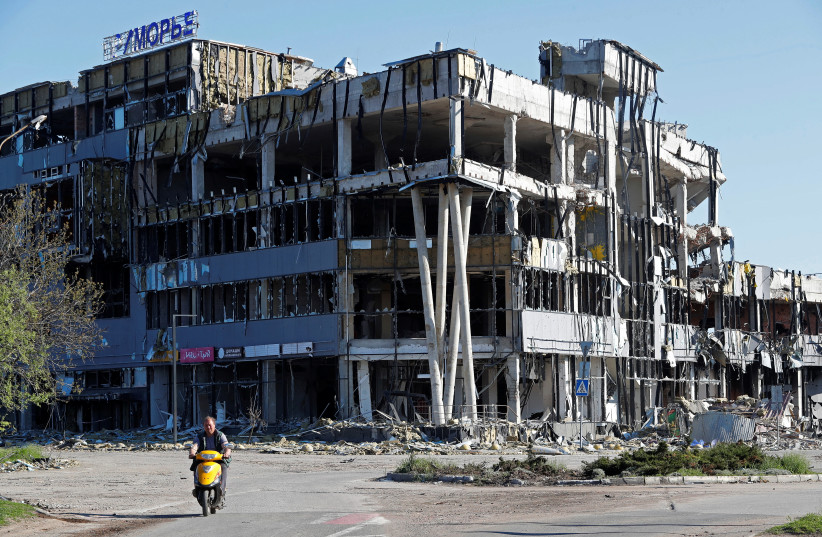  A local resident rides a scooter near a destroyed shopping mall in Mariupol. (photo credit: REUTERS/ALEXANDER ERMOCHENKO)