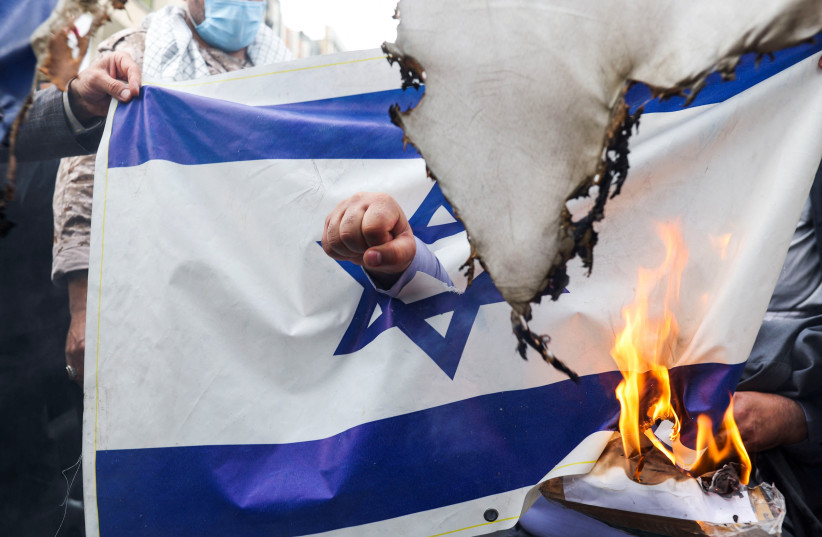  A protester punches his fist through an Israeli flag as Iranians burn flags during a rally marking the annual Quds Day, or Jerusalem Day, on the last Friday of the holy month of Ramadan in Tehran, Iran April 29, 2022 (photo credit: WANA NEWS AGENCY/REUTERS)