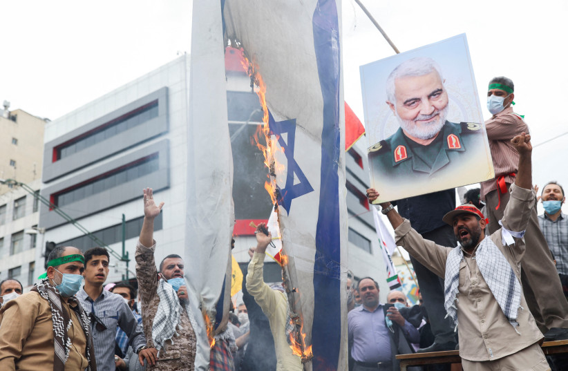 A man holds up a poster of the late Iranian Major-General Qassem Soleimani next to a burning Israeli flag as Iranians attend a rally marking the annual Quds Day, or Jerusalem Day, on the last Friday of the holy month of Ramadan in Tehran, Iran April 29, 2022 (credit: WANA NEWS AGENCY/REUTERS)