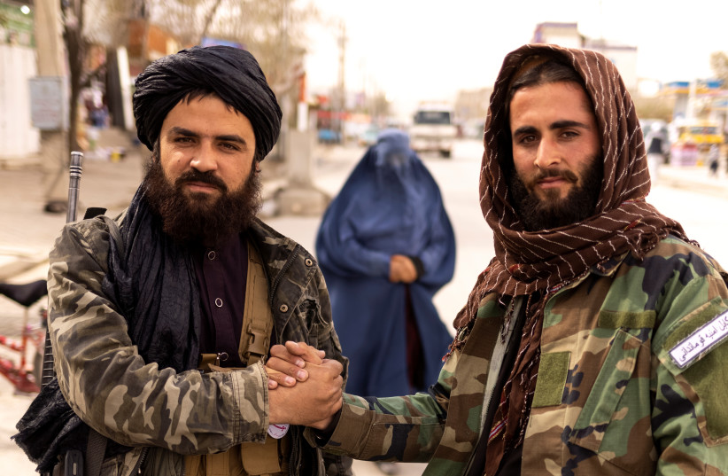  Taliban members Muhammad Aref and Junaid, greet each other at a checkpoint, as a woman in a burqa walks behind them, in Kabul, Afghanistan (photo credit: REUTERS/JORGE SILVA)