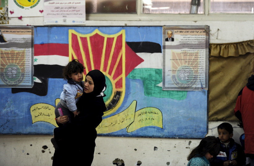 A Palestinian woman carrying a child, that fled from Yarmouk Camp, stand inside a school where they sought refuge in, during a visit by United Nations Relief and Works Agency (UNRWA) Commissioner-General Pierre Krahenbuhl (not pictured), in Tadamon neighbourhood south of Damascus April 12, 2015 (photo credit: OMAR SANADIKI/REUTERS)