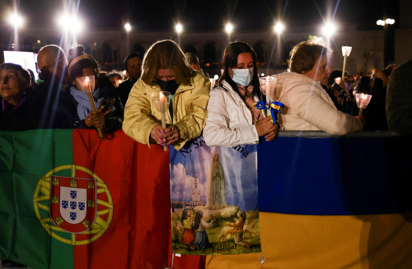  Pilgrims stand near the flags of Portugal and Ukraine as they attend an event marking the 105th anniversary of the reported appearance of the Virgin Mary to three shepherd children, at the Catholic shrine of Fatima, Portugal, May 12, 2022. (photo credit: PEDRO NUNES/REUTERS)