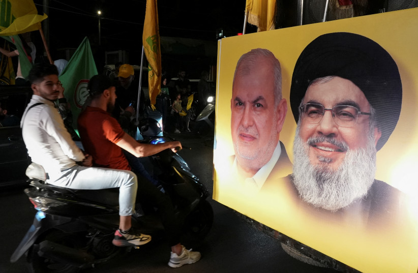  Supporters carry Hezbollah and Amal Movement flags as they ride in a convoy past a poster depicting Hezbollah leader Sayyed Hassan Nasrallah and parliamentary bloc head Mohamed Raad, as votes are being counted in Lebanon's parliamentary election, in Nabatiyeh, southern Lebanon May 15, 2022. (photo credit: REUTERS/ISSAM ABDALLAH)