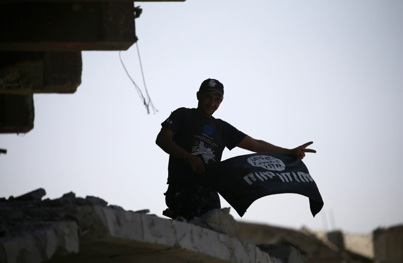  A member of Iraqi security forces celebrates as he holds a flag of Islamic State militants on the top of a destroyed building from clashes in the Old City of Mosul, Iraq July 10, 2017.  (credit: REUTERS/THAIER AL-SUDANI)
