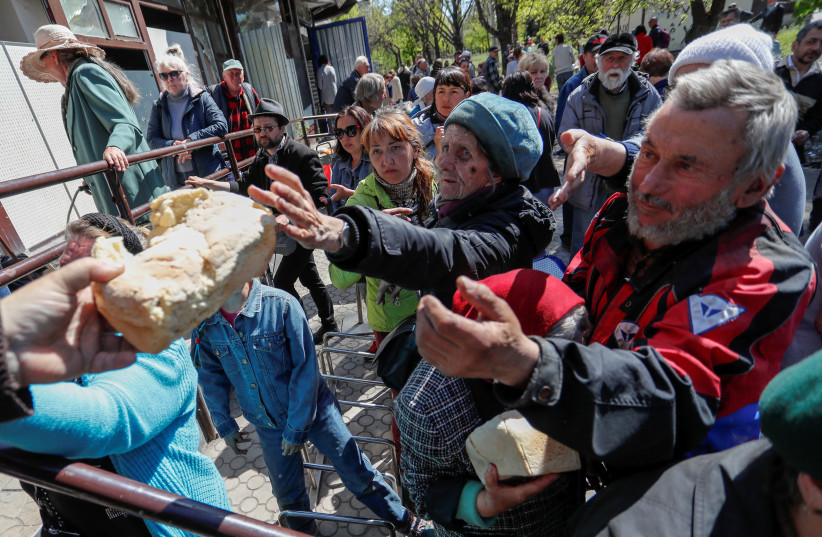  People receive bread during the distribution of humanitarian aid in the course of Ukraine-Russia conflict in the southern port city of Mariupol, Ukraine, on May 8, 2022.  (Alexander Ermochenko/Reuters) (photo credit: REUTERS/ALEXANDER ERMOCHENKO)