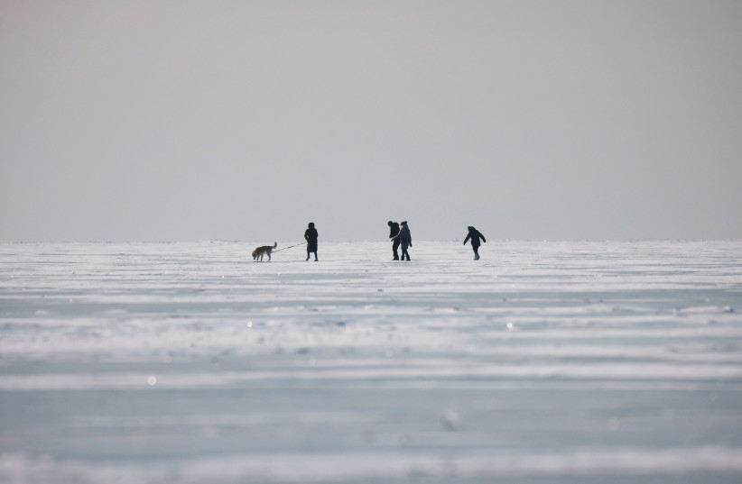  People walk with a dog on the frozen Lake Baikal in Irkutsk region (photo credit: REUTERS)