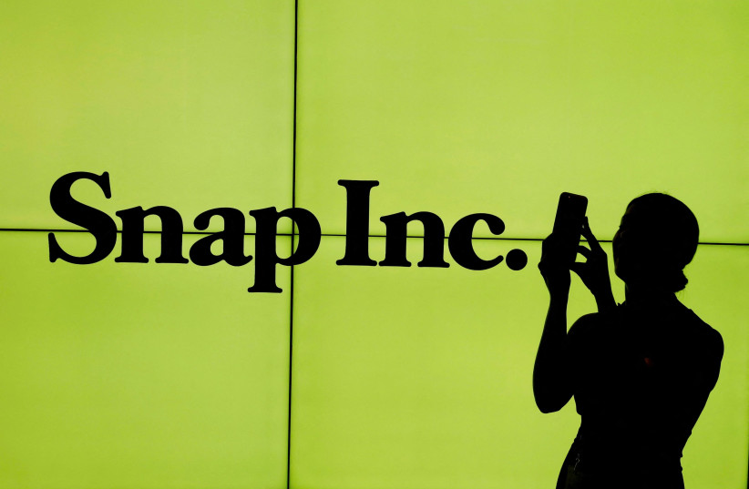 A woman stands in front of the logo of Snap Inc. on the floor of the New York Stock Exchange (NYSE) while waiting for Snap Inc. to post their IPO, in New York City, New York, US on March 2, 2017. (photo credit: REUTERS/LUCAS JACKSON/FILE PHOTO)