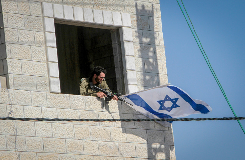 Israeli reserve soldiers guard near Israeli flag in the West Bank village of Hawara, near Nablus, May 26, 2022 (photo credit: NASSER ISHTAYEH/FLASH90)