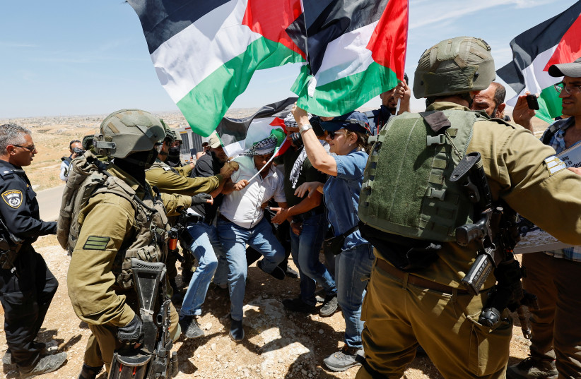 Israeli troops push people carrying Palestinians flags during a protest after Israeli top court paved way for razing eight Palestinian hamlets, in Masafer Yatta, south of Hebron, in the Israeli-occupied West Bank, May 20, 2022. (photo credit: REUTERS/MUSSA QAWASMA)