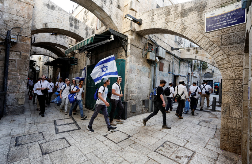  Jewish men carry Israeli national flags as they walk in an alley, inside Jerusalem's Old City, on Jerusalem Day, May 29, 2022. (credit: AMMAR AWAD/REUTERS)