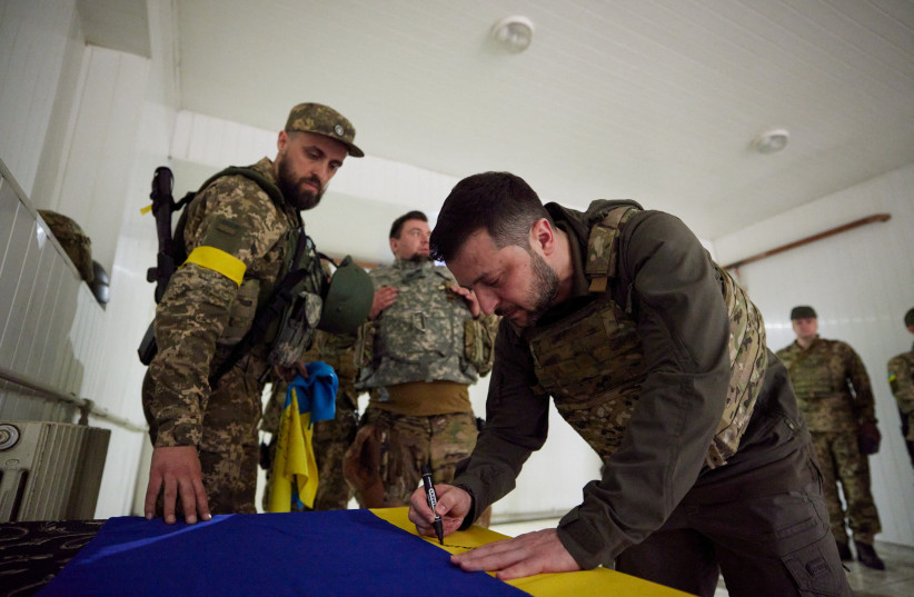 Ukraine's President Volodymyr Zelensky signs on a national flag as he visits a position of Ukrainian service members, as Russia's attack on Ukraine continues, in Kharkiv region, Ukraine May 29, 2022. (credit: REUTERS)