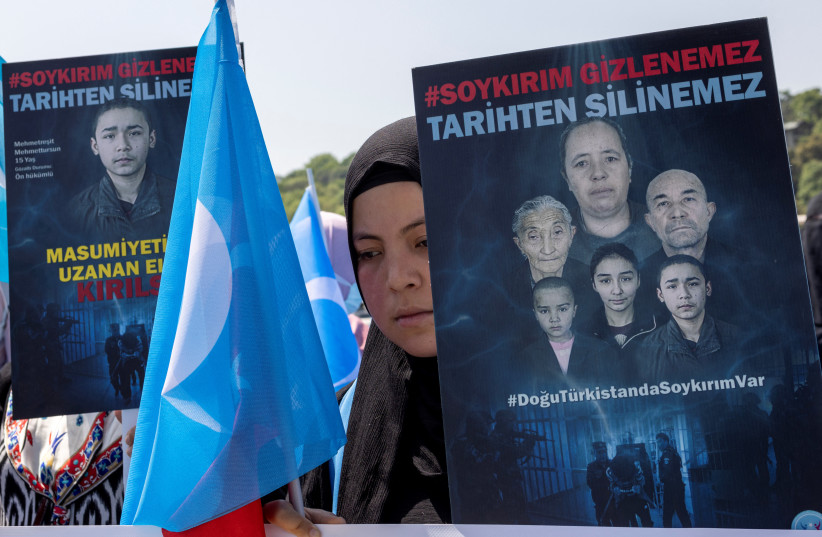  An ethnic Uyghur woman holds an East Turkestan flag and a placard that reads, "Genocide is undisguisable, can't be erased from history" during a protest against China near the Chinese Consulate in Istanbul, Turkey, May 26, 2022.  (photo credit: UMIT BEKTAS/REUTERS)