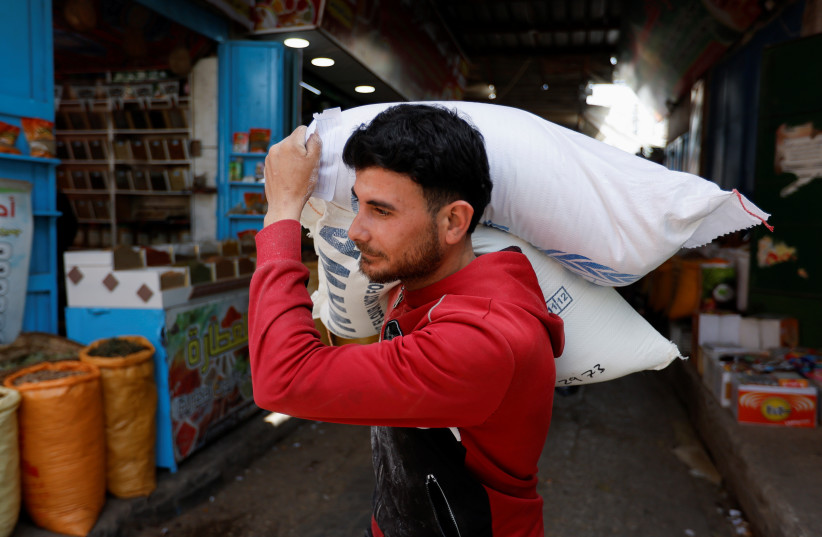  A Palestinian worker carries flour bags in a market during Ramadan in Khan Younis (photo credit:  REUTERS/Ibraheem Abu Mustafa)