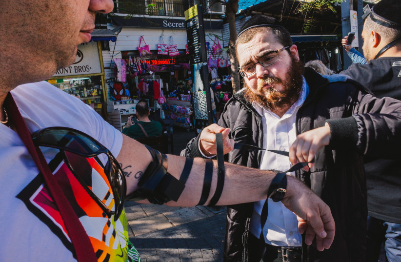  A Chabad emissary helps a man don tefillin at Tel Aviv’s Allenby Street, January 20, 2017. (photo credit: AMIR APPEL/FLICKR COMMONS VIA JTA)