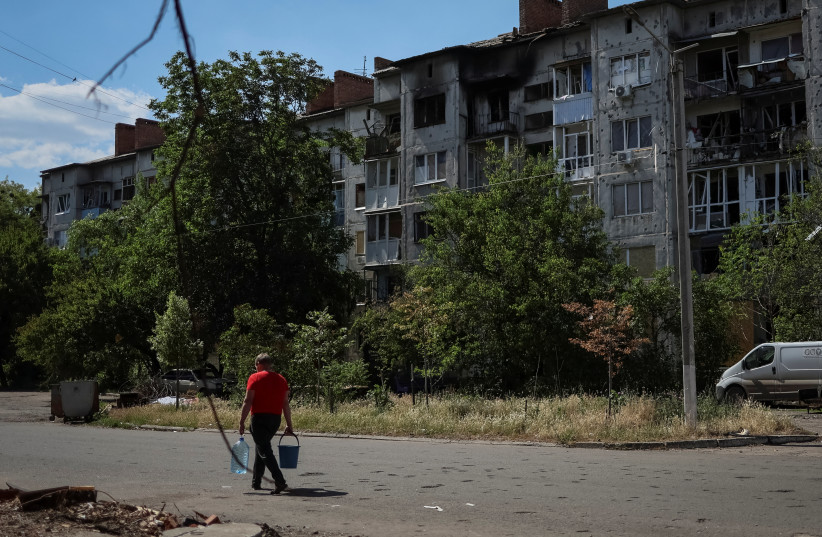 A local resident carries bottles with water in front of an apartment building destroyed in a missile strike, amid Russia's invasion of Ukraine, in Sloviansk, Ukraine June 7, 2022. (photo credit: REUTERS/GLEB GARANICH)