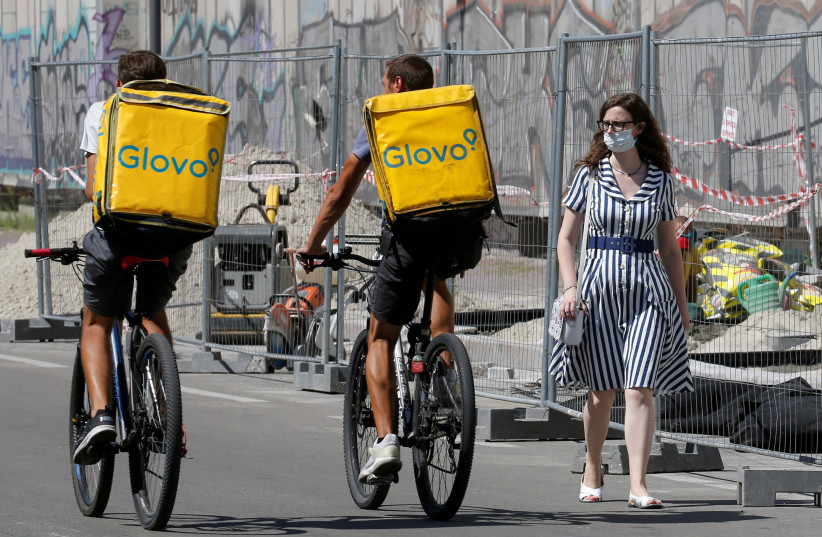  A woman wearing a protective face mask amid the outbreak of the coronavirus disease (COVID-19) walks past Glovo food delivery couriers in Kyiv, Ukraine August 6, 2020.  (credit: REUTERS/VALENTYN OGIRENKO)