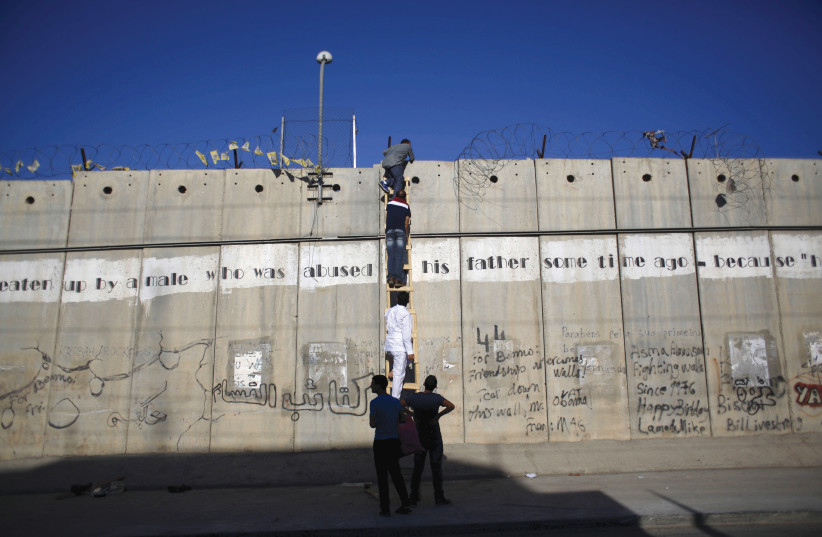  PALESTINIANS USE a ladder to climb over a section of the security barrier Al-Ram, near Ramallah, in 2015. (photo credit: MOHAMAD TOROKMAN/REUTERS)
