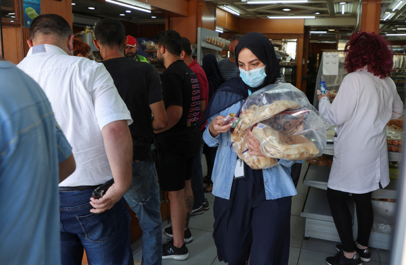 People queue as a woman carries several loafs of bread at a bakery in Beirut, Lebanon, June 29, 2022. (photo credit: REUTERS/MOHAMED AZAKIR)