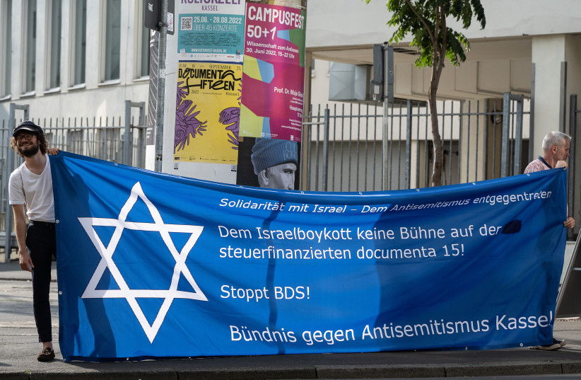 Demonstrators stand with a banner in front of the event hall before a panel event organized by the Anne Frank Educational Center and the Documenta art exhibition on the topic of “Anti-Semitism in Art,” Kassel, Germany, June 29, 2022. (credit: SWEN PFÖRTNER/PICTURE ALLIANCE VIA GETTY IMAGES)