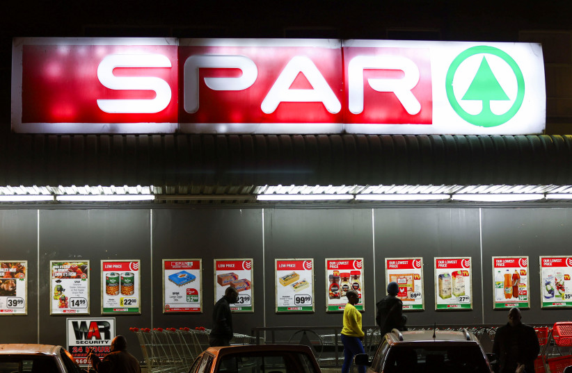  Customers walk beneath a company logo for the South African supermarket chain SPAR Group as they arrive at a supermarket in Johannesburg, South Africa, June 7, 2022. (photo credit: REUTERS/SIPHIWE SIBEKO)