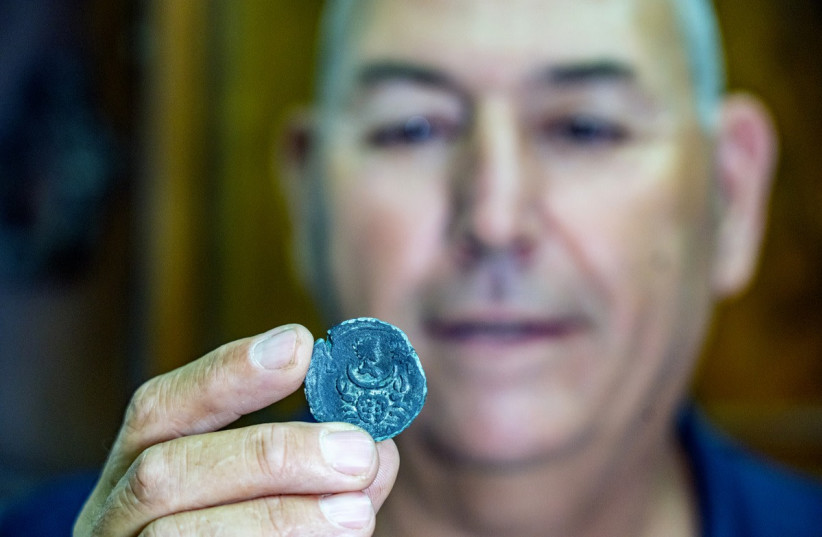  The 1,850-year-old bronze Roman coin found in Israel's waters is seen being held. It depicts the Cancer zodiac sign and the moon goddess Luna. (photo credit: DAFNA GAZIT/ISRAEL ANTIQUITIES AUTHORITY, YANIV BERMAN/ISRAELI ANTIQUITIES AUTHORITY)