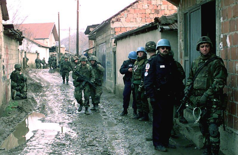  Soldiers from the US Army's Bravo Company, 3rd Battalion, 504th Parachute Infantry Regiment, and United Nations' police move down a muddy alley way in Mitrovica, Kosovo, in 2000. (credit: Wikimedia Commons)