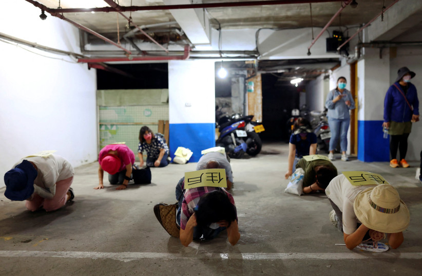  People demonstrate taking shelter with their hands covering their eyes and ears while keeping their mouth open, during a drill at a basement parking lot that will be used as an air-raid shelter in the event of an attack, in Taipei, Taiwan, July 22, 2022. (photo credit: REUTERS/ANN WANG)