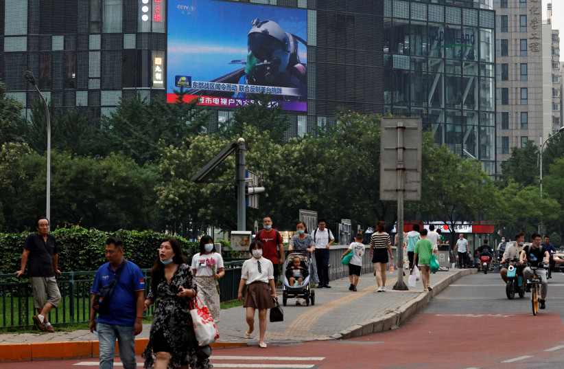 Pedestrians walk past a giant screen broadcasting news report on Chinese People's Liberation Army's (PLA) military exercises around Taiwan, in Beijing, China August 4, 2022. (credit: REUTERS/THOMAS PETER)