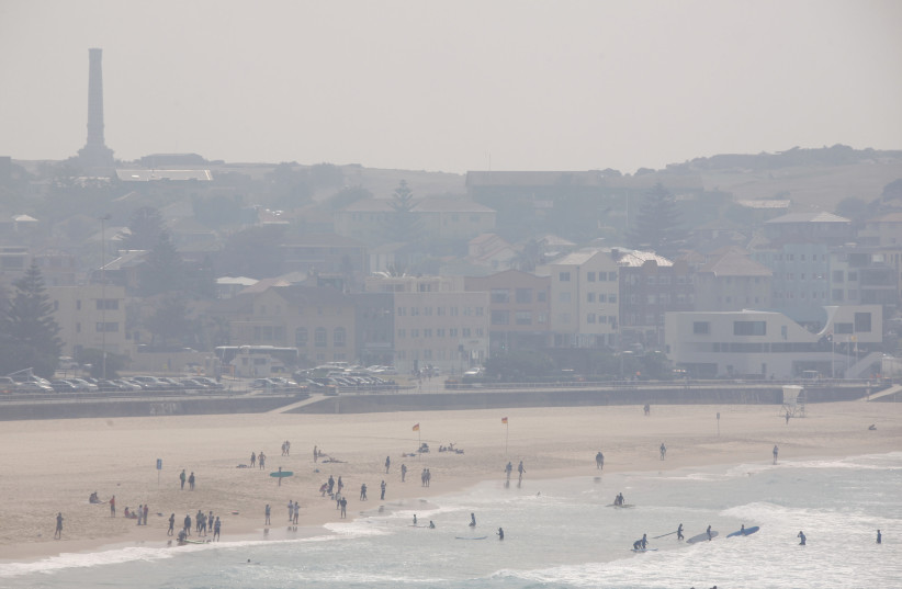  Surfers and swimmers are seen on Sydney's Bondi Beach October 29, 2013, as smoke from bushfires obscures the headland. Thick smoke, mainly from the bushfires that continue to burn in the Blue Mountains region, blanketed the city with around 60 fires still burning in the state of New South Wales. (credit: REUTERS/DAVID GRAY)