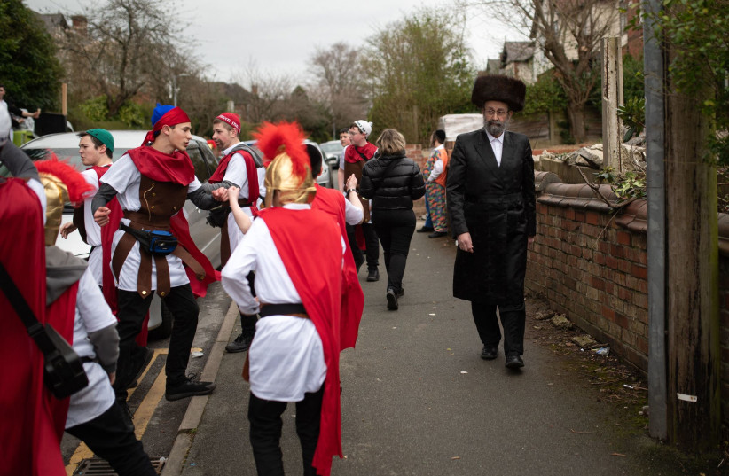  A man wearing haredi attire walks past Jews celebrating Purim in Manchester, UK, March 17, 2022. (photo credit: OLI SCARFF/AFP VIA GETTY IMAGES)