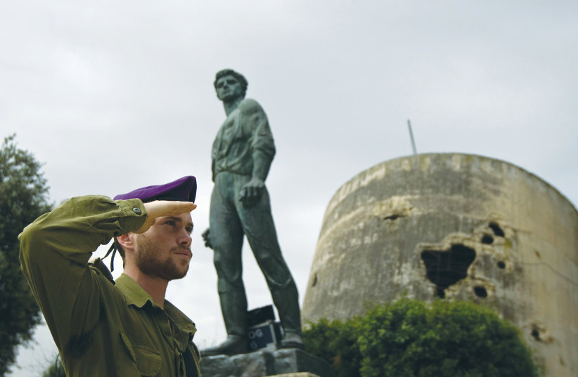  AN IDF officer salutes, at Kibbutz Yad Mordechai, in front of a statue of Mordechai Anielewicz, commander of the Warsaw Ghetto Uprising and the kibbutz’s old, destroyed water tower, as the nationwide siren to mark Holocaust Remembrance Day sounds, in 2011.  (photo credit: AMIR COHEN/REUTERS)
